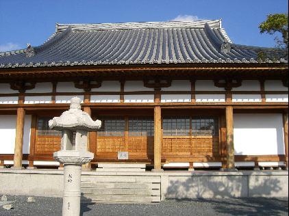 中央に茶色の引き戸があり、白い壁と瓦の屋根がある建物の写真
