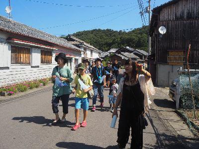 青空の下、子供も大人も帽子を被り先頭を歩いている女性の後をついて歩いている写真