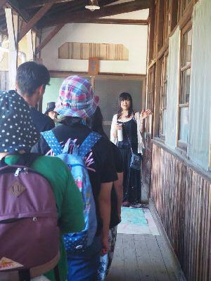 古い建物の中を参加者たちが並んで立ち、女性の話を聞いている写真