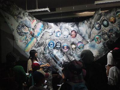 暗い室内に飾られた大きなクジラの作品を女性が説明している写真