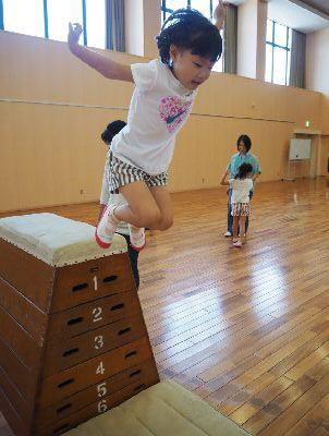 女の子が6段の跳び箱から両手を少し後ろに伸ばしてジャンプしている写真