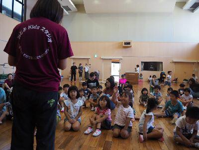 床に座っている子供たちの前にスタッフの方が立ち、1人の女の子が手を挙げている写真