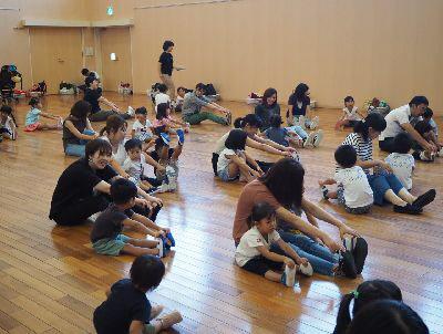 保護者の方と子供たちが足を伸ばして座り、手でつま先を掴んでいる写真