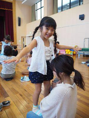お母さんの膝の上にバランスを取りながら立っている女の子の写真