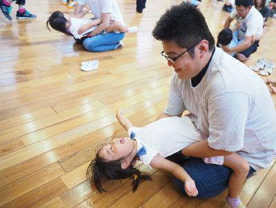 お父さんの膝の上に女の子が座って体を後ろに反っている写真