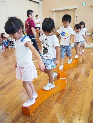 床に置かれたS字に曲がっている台の上を1列になってバランスを取りながら歩いている子供たちの写真