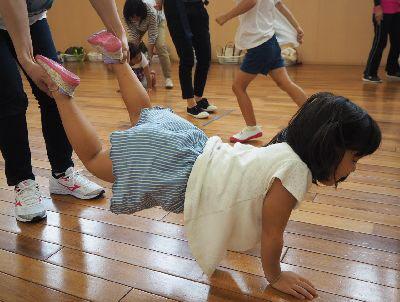 女の子が床の上に両手をついていて、大人が女の子の両足を持っている写真