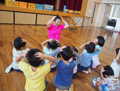 女性スタッフが両手を頭につけていて、集まっている子供たちも女性スタッフの真似をしている写真
