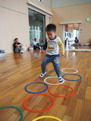 床の上に敷かれた色のついた丸の輪を男の子がケンケンパでジャンプしている写真