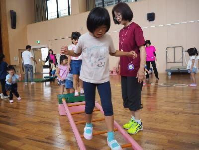 横に立てかけられた梯子の上を女の子が渡っている写真