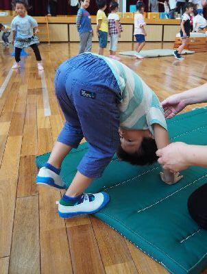緑のマットの上で男の子が前転をしようとマットに頭をつけている写真