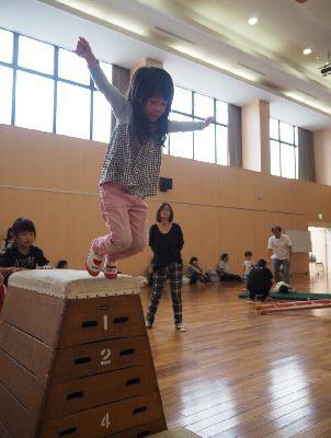 跳び箱の上から女の子が両手を広げてジャンプで降りようとしている写真