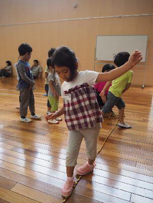 床の上にある細いロープの上を女の子が落ちないように歩いている写真