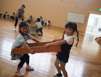 跳び箱の下段を女の子二人が向かい合わせで持って運んでいる写真