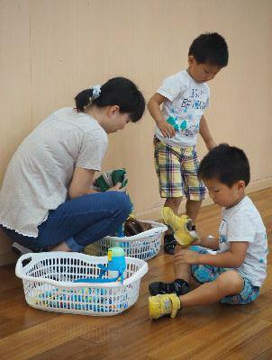 男の子二人とお母さんが写っており、白い籠にお母さんが靴を片づけており、右側に座っている男の子が黄色い靴を履いて準備をしている写真