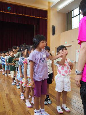 二人1組で手をつないで1列に並んでおり、先頭の女の子2組がスタッフの女性の前で握った手を肩の高さに挙げている写真