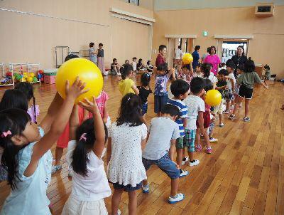 一列に並んでいる子ども達の頭の上を黄色いボールが次々と運ばれてきて、ボール送りゲームを楽しんでいる写真