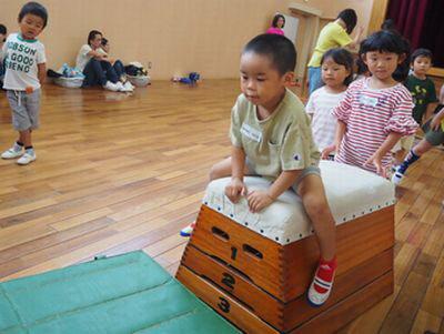 4段の跳び箱と体育マットが敷かれており、坊主頭の男の子が跳び箱にまたがっている写真