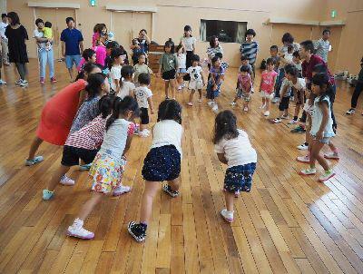 子ども達とスタッフの女性が円陣を作っており、片足を一歩前に出して両手を出した足の膝の上に置いて、上体を少し前に倒したポースを取っている写真