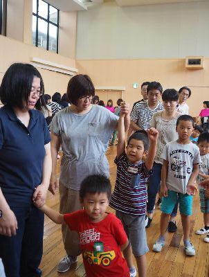 親子で手をつないで一列に並んでおり、青いティーシャツを着た男の子とお母さんが繋いだてを上に挙げている写真
