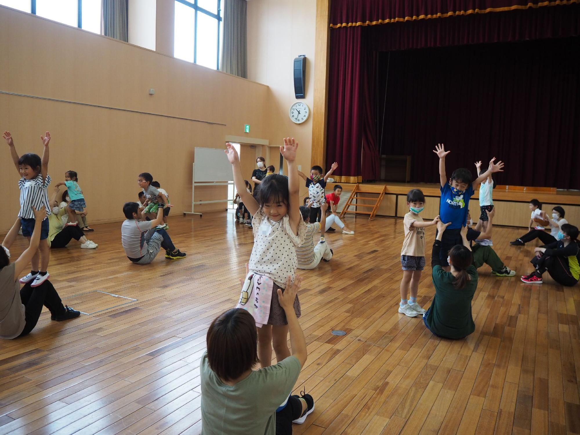 保護者のひざの上に立ちバンザイをする子どもたち