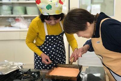 女性二人が卵焼き器でオレンジ色に色付けした生地を焼いている写真