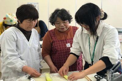 石井先生が焼いた生地をラップに包んで丸めている様子を見ている女性2人の写真