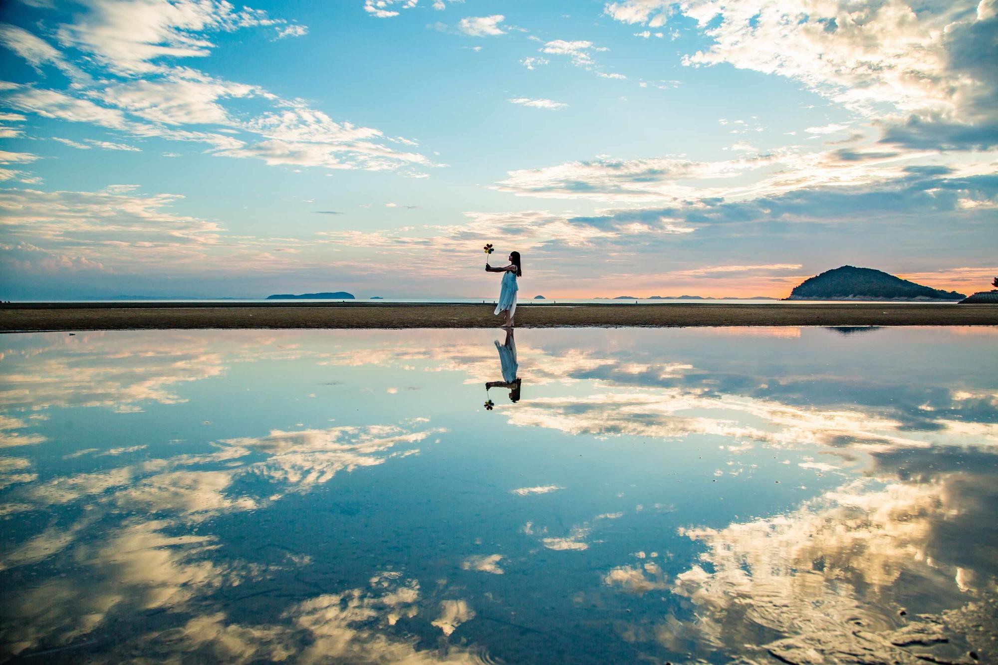 三豊市父母ケ浜の空がうつる水面に立つ女性の写真