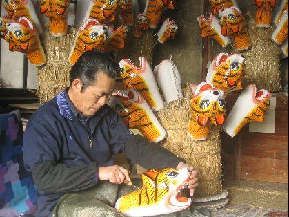 色付けされた張子虎の頭の仕上げ作業をしている三宅 修さんの写真