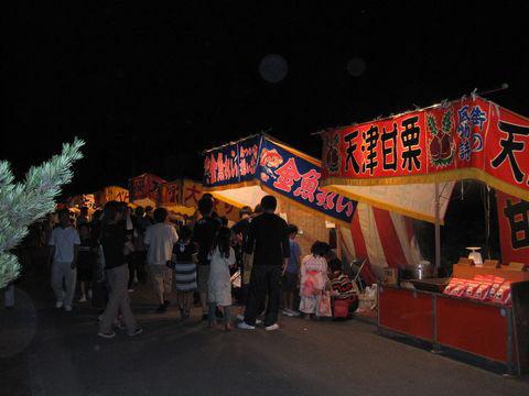 須賀神社の祇園祭にて灯りの灯った出店に人が賑わっている写真