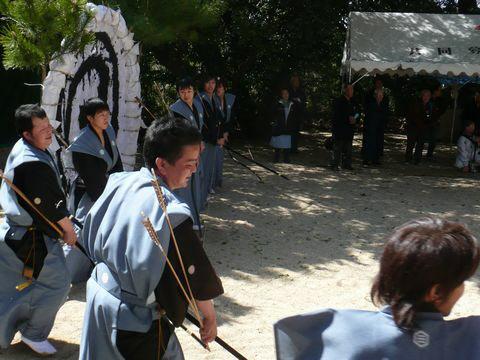 後ろには大きな丸い的があり、的の前に袴を着て弓と矢を持った人たちが並んでいる写真