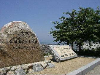 奥には木があり手前には大きな半円型の石で出来た記念碑が置かれている写真