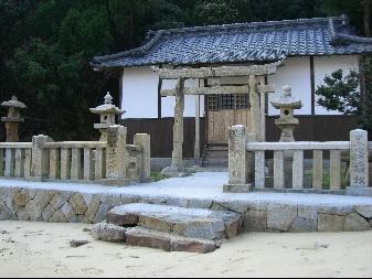 砂浜の上に石が敷き詰められている上に門や灯篭が立てられており、その後ろに鳥居と本殿がある浦島神社の写真