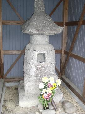 周りをトタンで囲まれ中に石造宝塔があり、菊の花が供えられてある写真