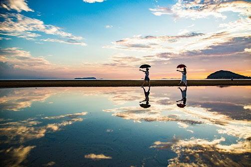 傘をさしている2名の女性が海に反射している夕暮れ時の美しい写真