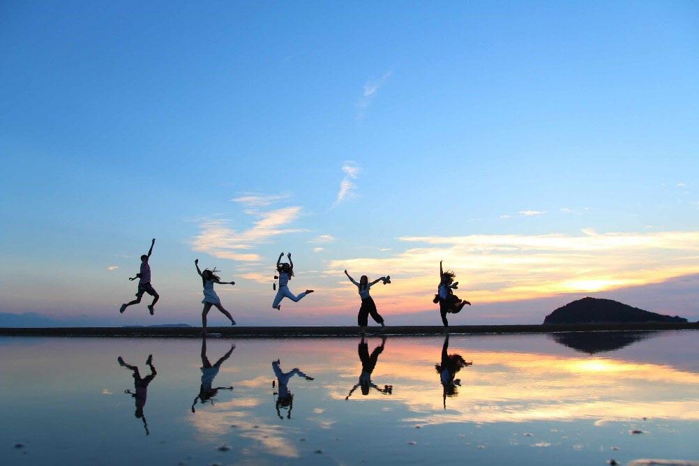 5名の男女が、父母ケ浜でジャンプして、水面に鏡のように映っている写真