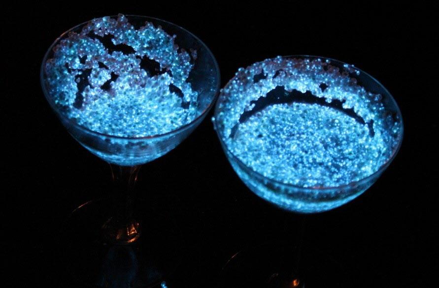暗闇で、2つのグラスの中で、ウミホタルが青い光を放っている写真