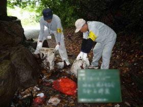 山中に不法投棄されたごみを片付けている職員2名の写真