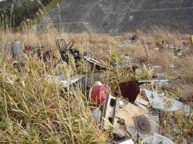 野原に金属の燃えないゴミなどが多数捨てられている写真