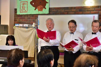 ミントクラブのメンバー3人の男性が手に持った赤いファイルを見ながら歌を歌っている写真