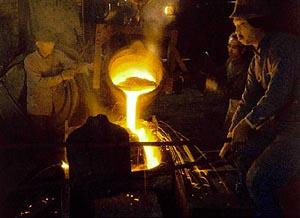 黄色に燃える溶解金属を流し込む作業をしている職人さん達の写真
