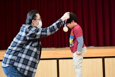 男の子が向かい合わせに立っているお父さんからメダルをかけられている写真