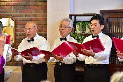3人のミントクラブの男性が手に赤いファイルを持ち歌を歌っている写真