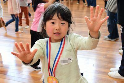 首にメダルをかけた女の子が両手を前にだしてハイタッチしようとしている写真