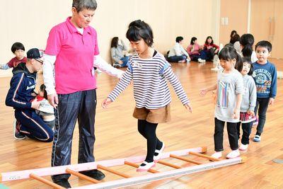 横に立てかけられた梯子の上を女の子が歩いている写真