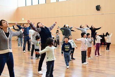 参加者の親子たちが腕を大きく横に広げて体操をしている写真