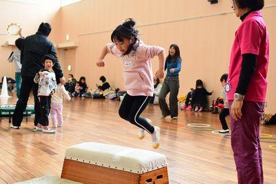 ピンクの服を着た女の子が一段の跳び箱を両足ジャンプで飛び越えようとしている写真
