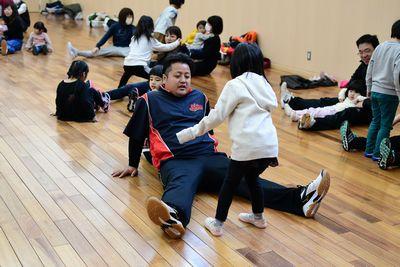 お父さんが床に座って足を広げて伸ばしていてその間に女の子が立っている写真