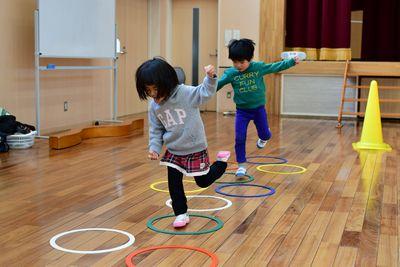 床の上に置かれた丸の上を子供たちがケンケンパしながらジャンプしている写真
