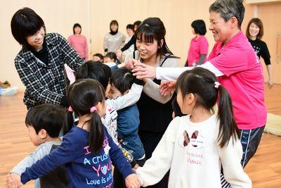 子どもやお母さんたちが片手ずつ違う人と手をつないで丸く集まっている写真